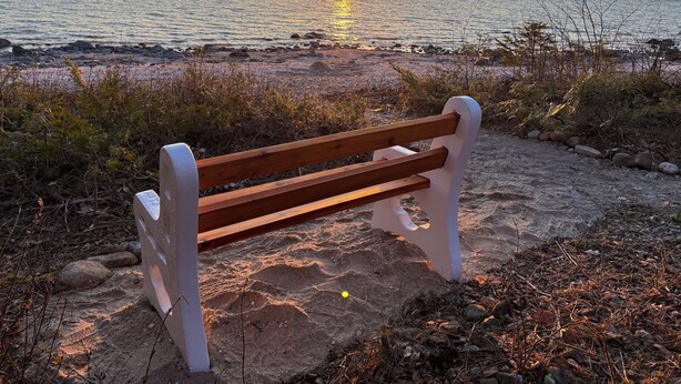 Un banco de madera sobre una playa arenosa con una puesta de sol al fondo.