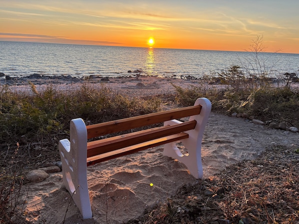 Un banco de madera sobre una playa arenosa con una puesta de sol al fondo.
