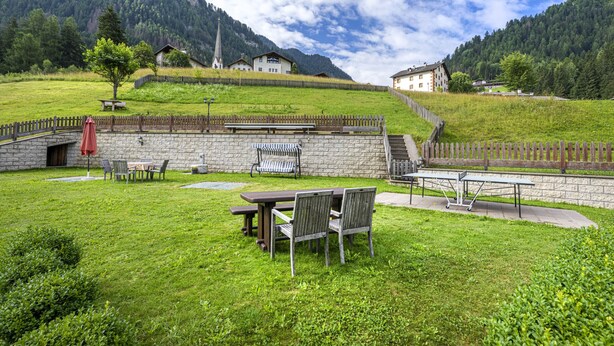 Un’area verde con tavoli e sedie da picnic, un muro in pietra e una recinzione in legno.