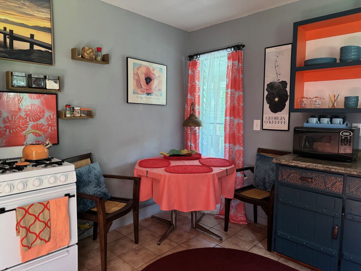 Uma cozinha com fogão, mesa com toalha vermelha, cadeiras e armário.