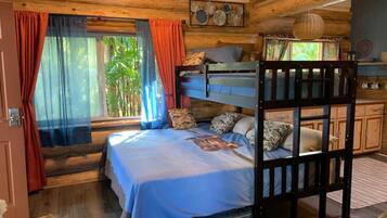 A rustic wooden cabin bedroom with a bunk bed, a large window with curtains, and a view of greenery outside.