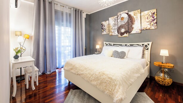 A bedroom with a large bed, a desk, and a chair, a bedside table with a lamp, and a wall with three paintings.