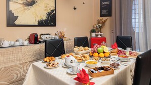 A dining table set with various breakfast items, including pastries, fruits, and beverages, in a room with patterned wallpaper and a large abstract painting on the wall.