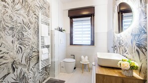 A bathroom with a shower, toilet, sink, and a window with blinds.