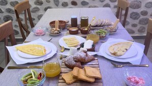 Une table dressée avec des aliments pour le petit-déjeuner, notamment des viennoiseries, des fruits et des boissons, avec un mur de pierre en arrière-plan.