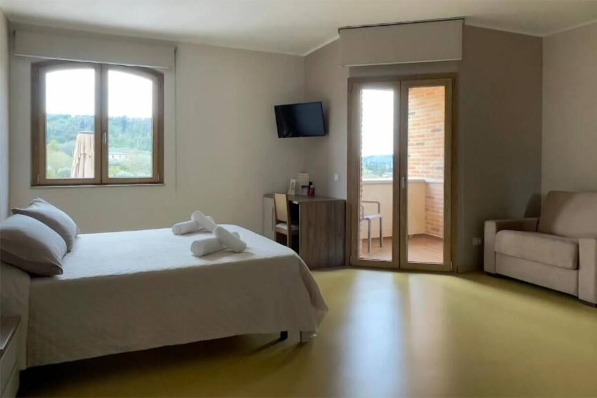 Una camera d'hotel con un letto, una sedia, una scrivania, una TV e un balcone con vista.