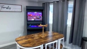 A modern living room with a wooden dining table, white metal frame, and a flat-screen TV mounted on the wall. - Welcome to The Cozy Cove, Your Lakeside Retreat (Havasu Lake)