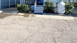 A single-story building with a covered porch, a flagpole with an American flag, and a large water tank in the front yard. - Welcome to The Cozy Cove, Your Lakeside Retreat (Havasu Lake)