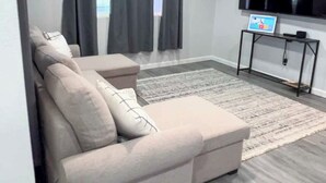 A modern living room with a sectional sofa, a flat-screen TV, and a small table. - Welcome to The Cozy Cove, Your Lakeside Retreat (Havasu Lake)