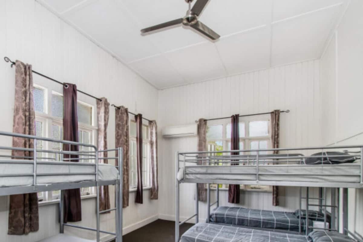Une chambre de dortoir avec des lits superposés, un ventilateur de plafond et des rideaux aux fenêtres.