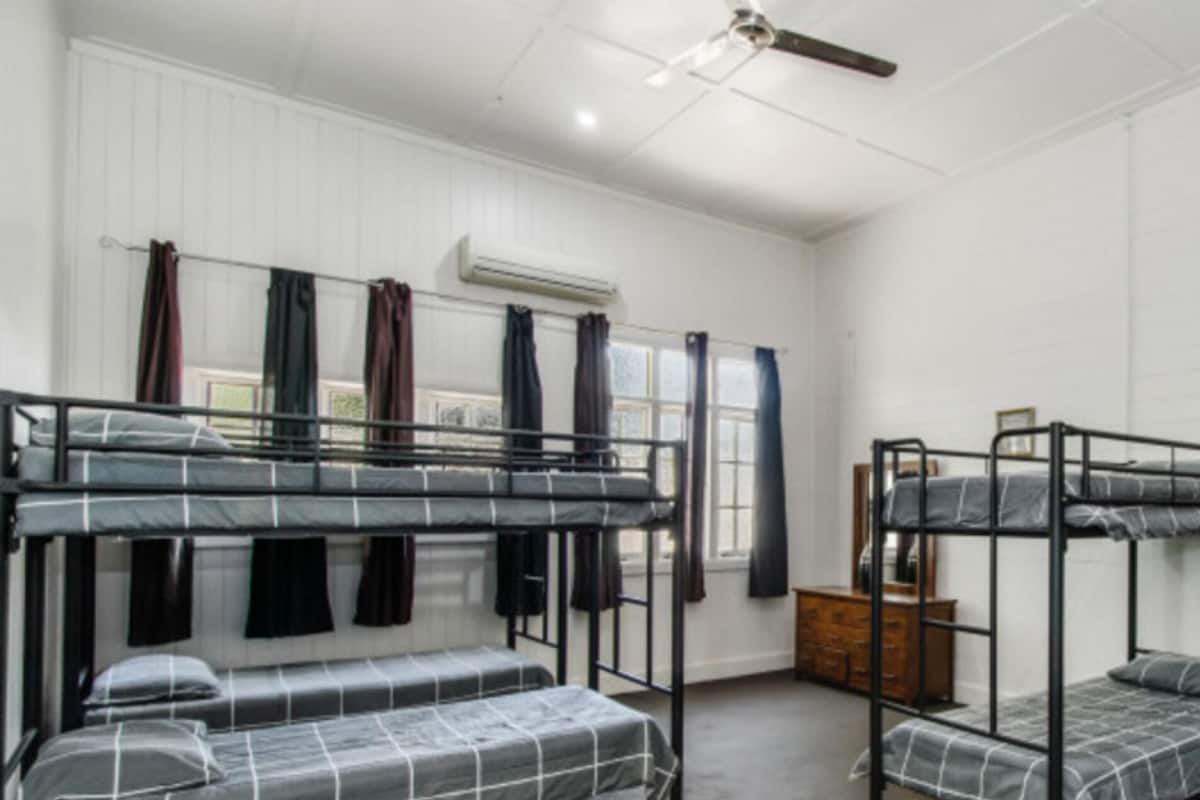 Une chambre de dortoir avec des lits superposés, un ventilateur de plafond et une fenêtre avec des rideaux.