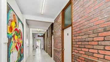 A hallway with a brick wall, a door labeled '6', and a colorful abstract painting on the wall.