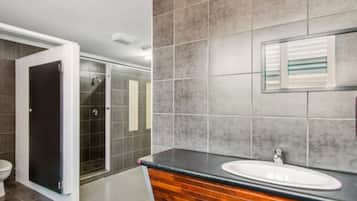Un baño moderno con tocador de madera, un espejo grande y zona de ducha.