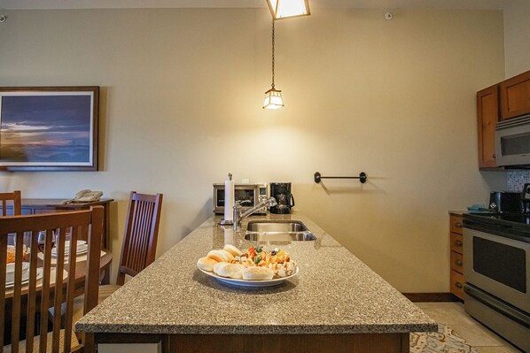 A kitchen with granite countertops, a dining area with wooden chairs, a microwave, a coffee maker, and a hanging light fixture. - Soaring Eagle 414, Studio (Snowshoe)