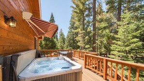 A wooden deck with a hot tub, outdoor furniture, and a view of a forest.