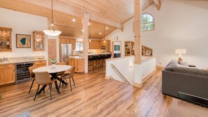 A spacious kitchen with wooden cabinets, a dining area with a round table and chairs, and a living area with a sofa and lamp.
