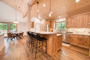 A spacious kitchen with wooden cabinets, a granite countertop, and a central island with bar stools. - Knotty and Nice by Tahoe Getaways - 4BR + Hot Tub -Close to Lake! (Tahoe Vista)