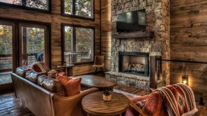 Una sala de estar acogedora con chimenea de piedra, sofás de cuero y grandes ventanas con vistas al exterior.