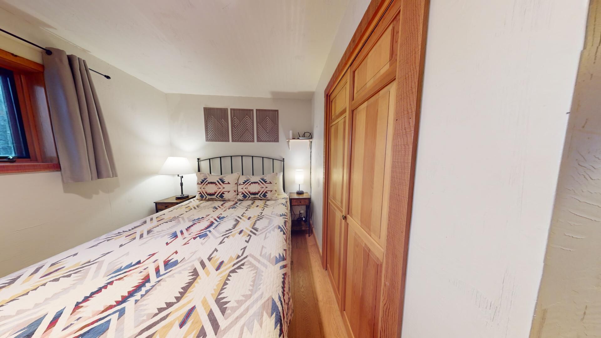 A bedroom with a bed, bedside lamps, a wooden wardrobe, and a window with curtains.
