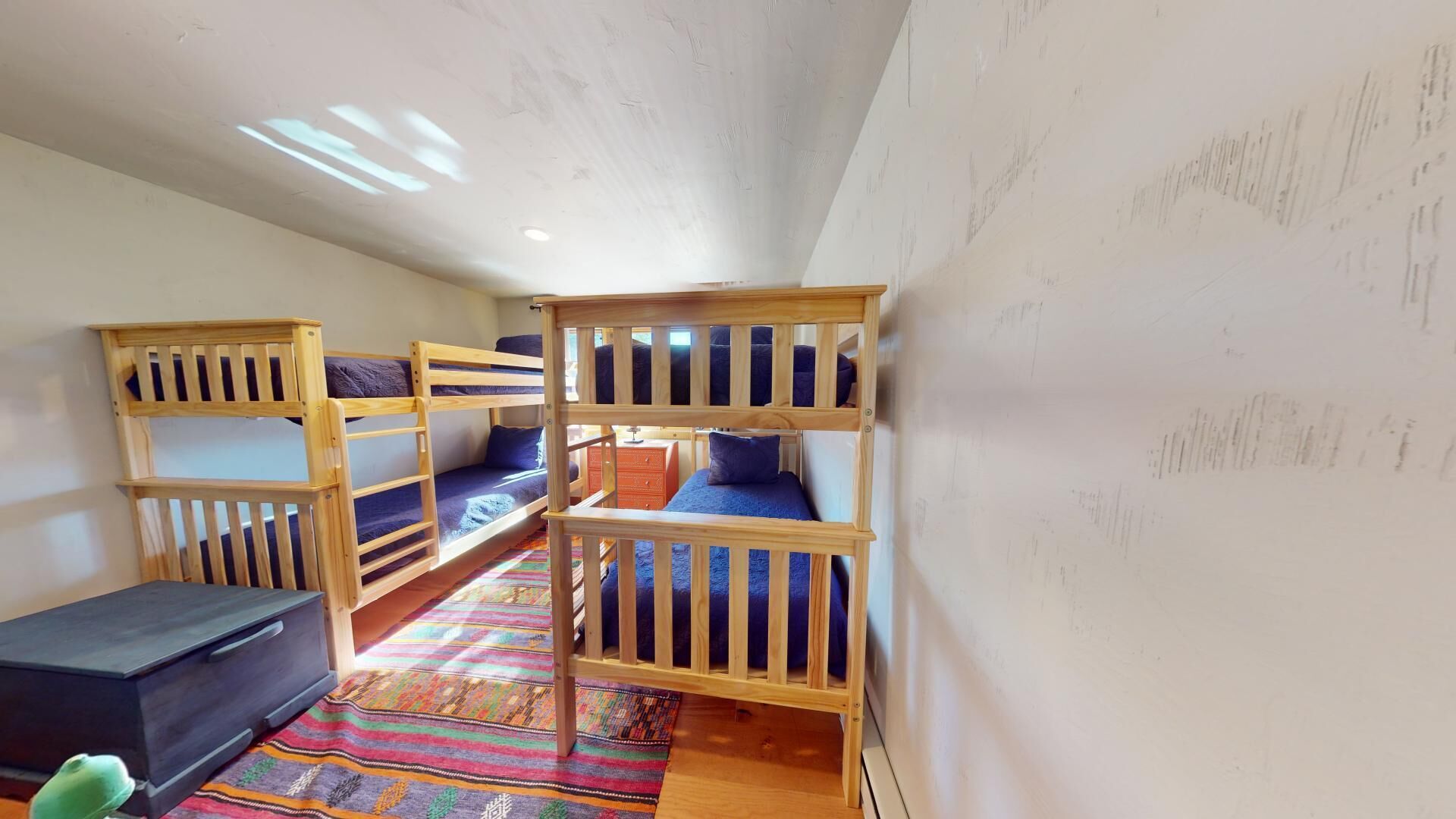 A dormitory room with bunk beds, a small desk, and a colorful rug.