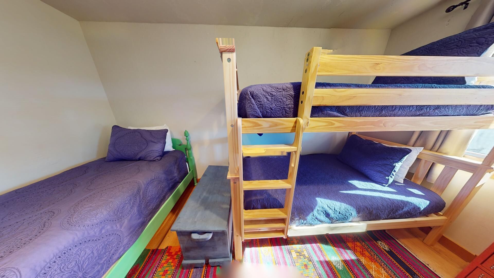 Quarto com beliche, escada, um banco e um tapete colorido.