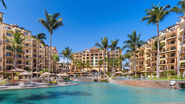 Ein Resort mit einem zentralen Pool, zahlreichen Palmen und einem großzügigen Gebäude mit Balkonen.