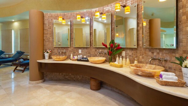 A modern bathroom with a curved vanity, multiple mirrors, and a large sink. - Villa del Palmar Flamingos Resort & Spa (Nuevo Nayarit)