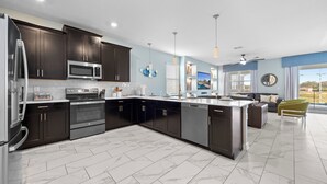 A modern kitchen with dark cabinets, stainless steel appliances, and a marble floor.