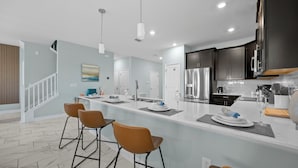 A modern kitchen with a central island, bar stools, stainless steel appliances, and a herringbone-patterned floor.