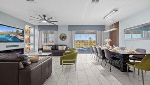 A modern living room with a sofa, a dining area with a table set for six, and a large window overlooking a pool.