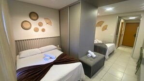 A hotel room with a bed, a bench, and a small table with towels. There are wall decorations and a door in the background. - Flat 211 Vista Mar EcoResort by La Playa (Tamandaré)