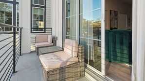 A balcony with wicker furniture, a glass door, and a view of the outdoors. - The Houston Hangout: Modern Comfort & Style (Houston)