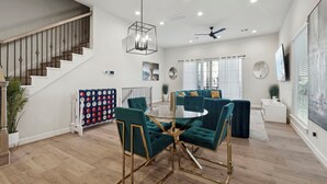 A spacious living area with a staircase, a round glass table with chairs, and a green sofa set. - The Houston Hangout: Modern Comfort & Style (Houston)