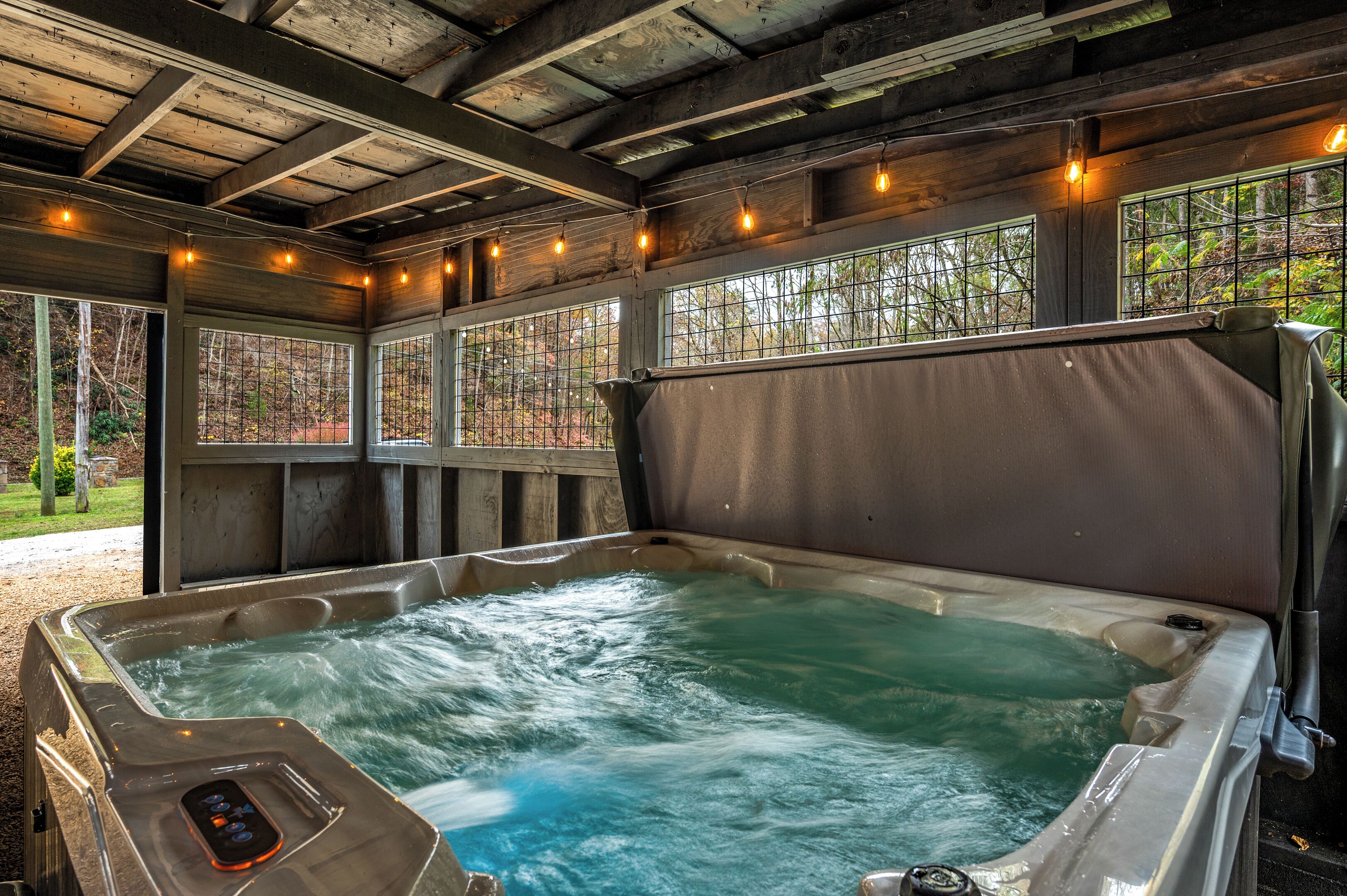 A hot tub with a control panel, surrounded by wooden beams and windows with metal grilles.