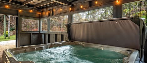 A hot tub with a control panel, surrounded by wooden beams and windows with metal grilles.