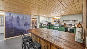 A modern kitchen with wooden ceiling, green cabinets, and a large island with bar stools. - Location! ★ Game R. ★ Movie R. ★ Hot Tub ★ Fire Pit ★ King Beds ★ Dollywood! (Sevierville)