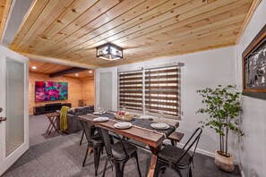 A dining area with a wooden table, chairs, and a television in the background.