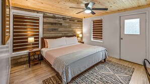 A bedroom with a wooden ceiling, a bed with a striped bedspread, two bedside lamps, and a window with blinds. - Location! ★ Game R. ★ Movie R. ★ Hot Tub ★ Fire Pit ★ King Beds ★ Dollywood! (Sevierville)