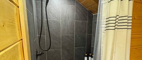 Uma área de chuveiro com piso em azulejos, um chuveiro e uma cortina.