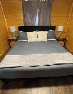Una stanza con rivestimento in legno, un letto, due comodini con lampade e una finestra con tende.