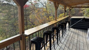 Eine Holzterrasse mit Geländer, schwarzen Barhocker und einer schwarzen Couch.