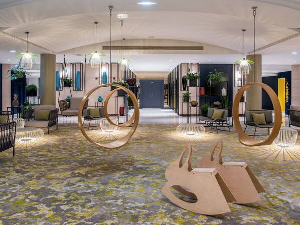 A spacious lobby with modern furniture, hanging light fixtures, and a patterned carpet.