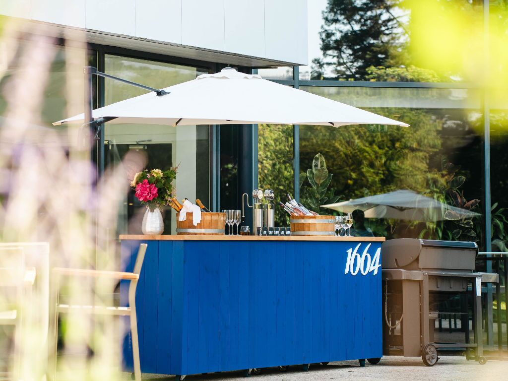 A blue outdoor bar area with a number 1664, a white umbrella, and a grill.