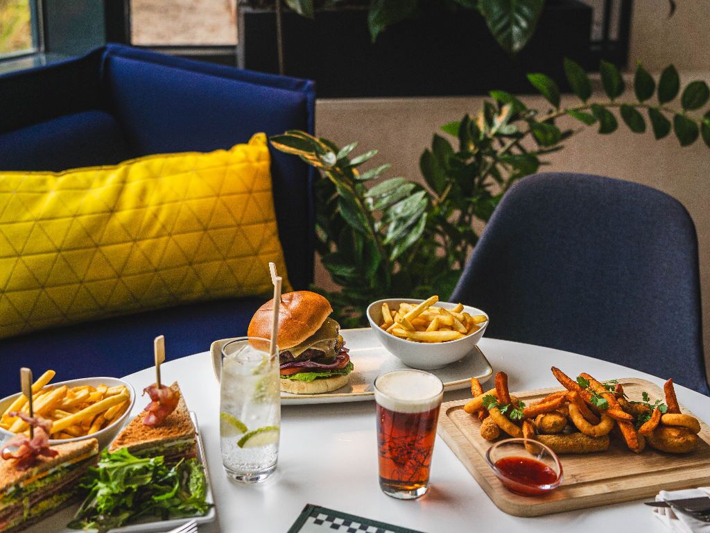 Una mesa de comedor con una hamburguesa, papas fritas, un sándwich y una bebida.