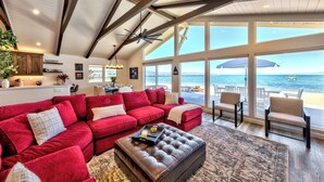 A spacious living room with a red sectional sofa, a leather ottoman, and a view of the ocean through large windows.