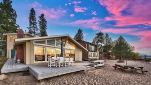 A modern beach house with a large deck, outdoor seating, and a scenic view of the ocean and mountains.
