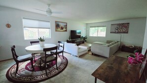Ein Wohnzimmer mit einem runden Esstisch, zwei Sofas, einem Fernseher und einem Deckenventilator.