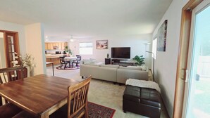 Ein modernes Wohnzimmer mit einer Couch, einem Fernseher und einem Essbereich mit Stühlen und einem Tisch.