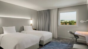 A hotel room with two beds, a desk, and a view of the outdoors. - Chambre Deluxe près de CDG + Navette gratuite (Le Mesnil-Amelot)