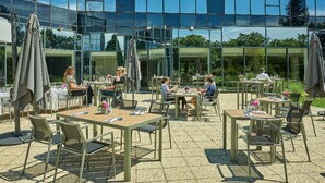 An outdoor patio area with tables and chairs, surrounded by a glass building reflecting the sky.